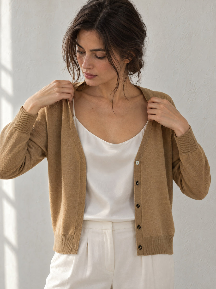 Woman sliding the camel cardigan over her shoulders in soft window light